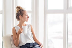 A mom looking content looking out the window with her cup of tea. She is processing things that she would not normally share with people. Marble Wellness is a counseling practice in Chicago and offers counseling to working moms.