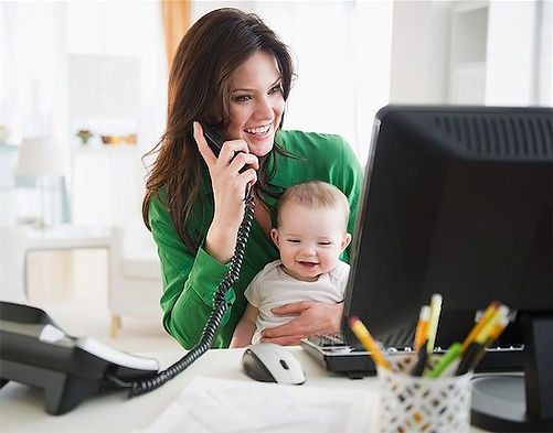 A mother smiling while holding her baby and working from home. Therapy can help moms who are juggling it all. Marble Wellness is located in Chicago and offers counseling services for working mothers. 