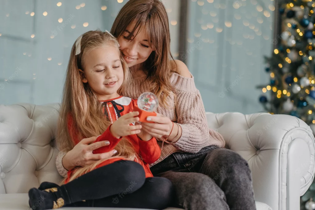 A mother sitting with her young daughter smiling at a snow globe with her. The mom is truly present and enjoying the holidays. Marble Wellness specializes in Therapy for Moms. 