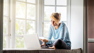 A woman sitting crossed legged comfortably in her own home doing online therapy by her favorite window. Marble Wellness offers Online Therapy for women in Missouri.