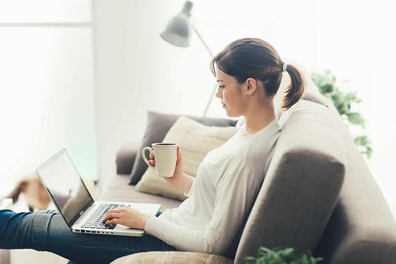 A woman on her computer doing virtual online therapy with her therapist. She is comfortable in her own home, on her couch, drinking tea. Marble Wellness offers Online Therapy for Men and Women in Missouri.