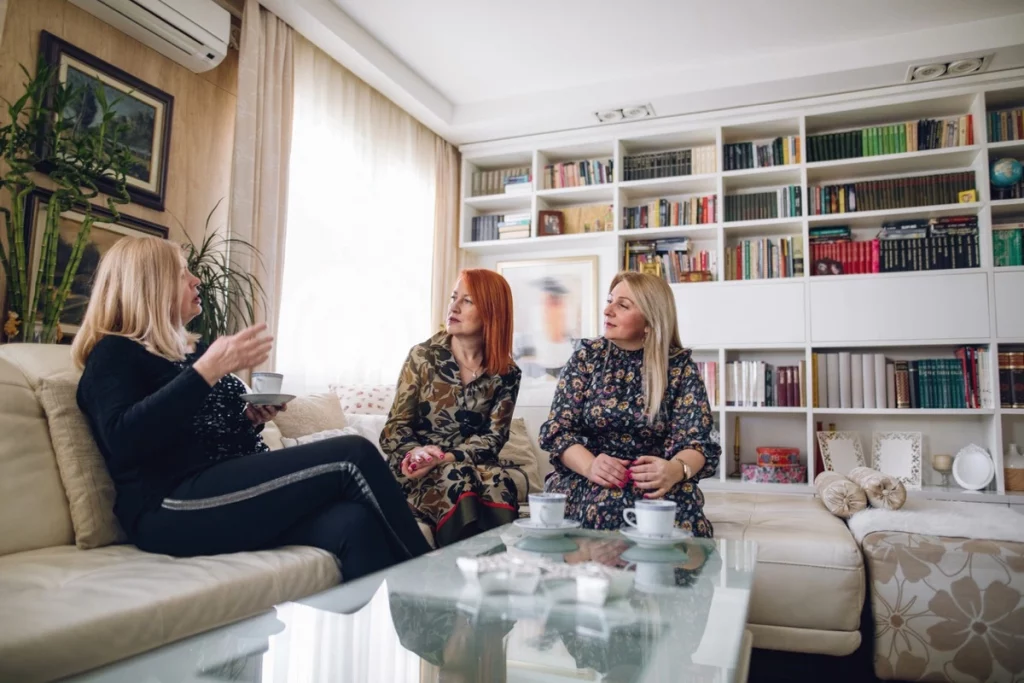 Three adult sisters talking on a couch having a serious conversation about duties for taking care of their parents. Marble Wellness is a Counseling practice in STL offering family and individual counseling to help navigate life transitions.  