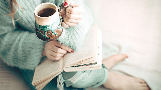 A mother cozy on the couch reading a book and drinking coffee. She appears calm. Marble Wellness is located in Chicago, IL and offers therapy to mothers who are looking to find calm and balance in their lives. Marble Wellness offers in person or virtual therapy. 