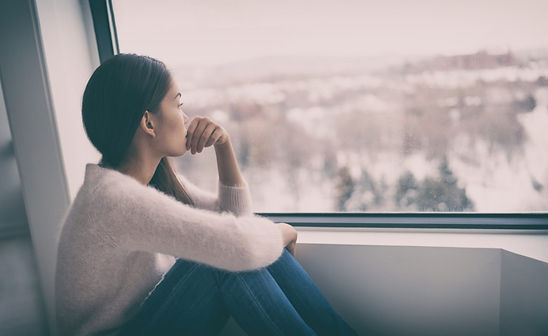 A woman looking out the window looking sad and thinking. She appears to be depressed. Marble Wellness is a counseling practice offering therapy to moms in Chicago looking to improve their mental health. Marble Wellness offers in person or virtual therapy.