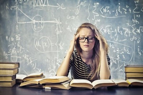 A teen girl behind school books and looking stressed. Marble Wellness offers Teen Counseling either in person or virtually.