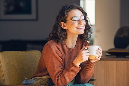 A woman sitting on her couch smiling and enjoying a cup of tea. Self care if so important. Marble Wellness is a mental health therapy practice and is dedicated to getting you through challenging times so you can focus on yourself and feeling better. 