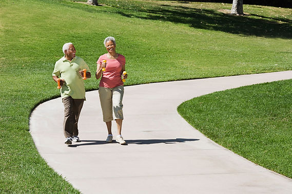 A couple walks on a sidewalk in a park. Walking has many mental health benefits and is good to pair with therapy.