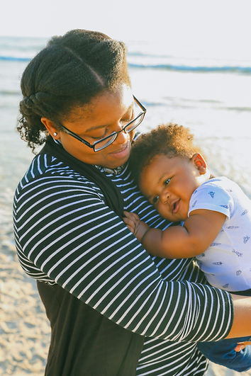 A mom takes a walk with her baby on the beach. Marble Wellness therapists specialize in moms in St. Louis and Chicago and can help with postpartum depression and postpartum anxiety.