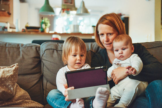 A mom looks at an iPad with her baby and toddler. Moms can find a therapist in St. Louis  at Marble Wellness to start therapy for moms, therapy for men, therapy for kids, therapy for teens, and couples therapy.