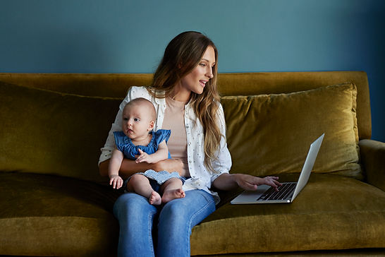 A mom holds her baby on a couch. Moms can find a therapist near me at Marble Wellness in St. Louis, MO 63011 to overcome mom guilt.