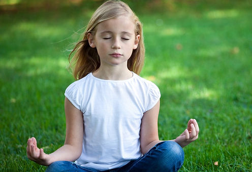 A girl practices meditation while sitting in the grass. Therapists at Marble Wellness in STL help children develop calming  techniques like deep breathing and meditation.