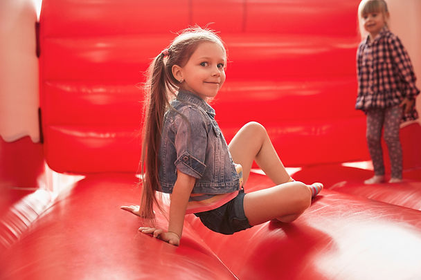A girl bounces in a red bouncy house. Marble Wellness in St Louis is a therapist near me that offers play therapy, therapy for teens, and therapy for moms and dads.