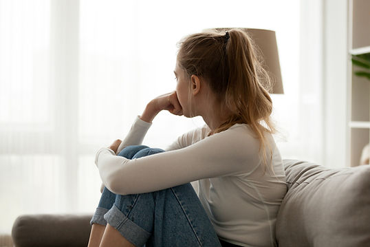 A woman on a couch looks away sadly. Marble Wellness in St. Louis, MO offers therapy for miscarriage and other concerns related to pregnancy, infertility, and stillbirth.