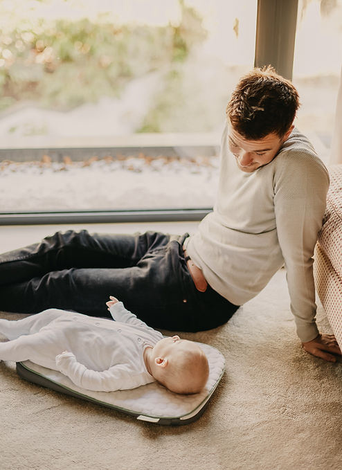 A dad watches his baby lying on a mat on the floor. Therapy for men in St. Louis can help ease the transition into parenthood. Skyler Martin, a therapist at Marble Wellness in Ballwin, MO 63011 specializes in therapy for dads.