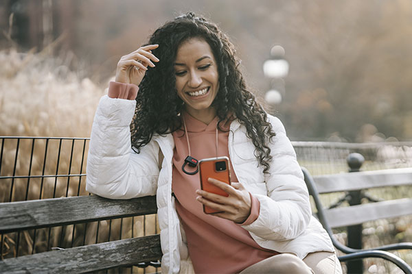 Photo of a woman sitting on a garden bench holding a smartphone and laughing. Breakup recovery in Chicago, IL | therapy for breakups in Chicago, IL | relationship therapy for singles | relationship therapist | 63122 | forrest glen 60630 | Lincoln Park is 60614 | north center 60613 | 6061.