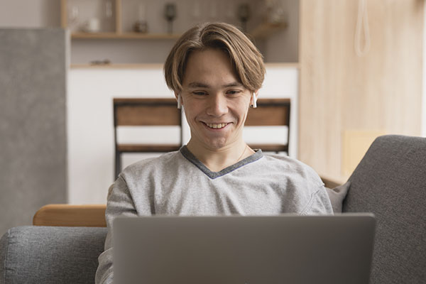 Photo of a young man on the sofa smiling at his computer doing online therapy in Missouri with a licensed online therapist in Missouri. St. Louis based Marble Wellness provides online counseling in Missouri for depression, anxiety, men, and more.