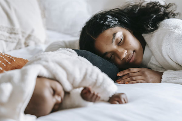 Photo of a mother and her baby sleeping in bed. Counseling for moms in St. Louis, MO is here as well as counseling for postpartum in St. Louis and online counseling for women in Missouri! Get the postpartum support you need!