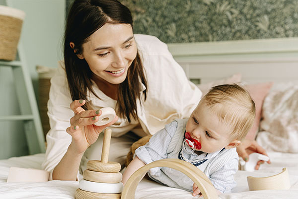 Photo of a mother and baby boy playing with a wooden toy. Counseling for moms in St. Louis, MO is here as well as postpartum support in St. Louis and online counseling for women in Missouri! We can help you.