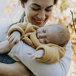 Photo of a smiling woman looking at her sleeping baby. You can feel better in postpartum care with postpartum counseling in St.Louis, MO at Marble Wellness.
