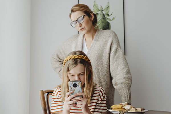 Photo of a mother looking at her daughter with a worried expression while she is on her phone. Parenting teens is hard! Get counseling for moms of teens St. Louis, MO with an STL therapist. Get the help you need with online therapy in Missouri and online counseling in St. Louis, MO creating good memories together.