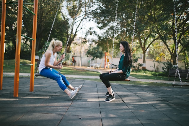 Two girls facing each other on park swings. Sharing your grief journey with loved ones or through support groups helps in processing emotions. Find a St. Louis counselor today.