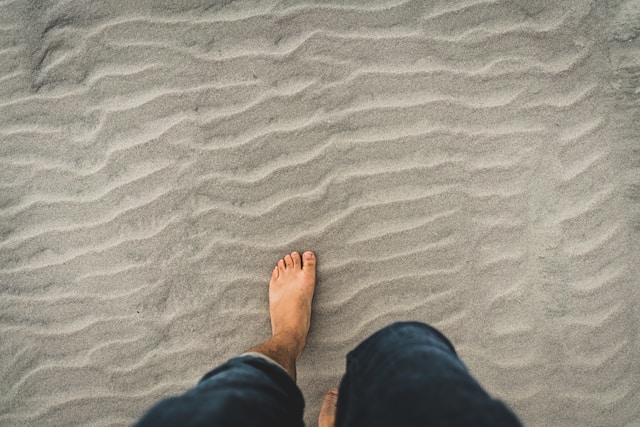 Jeans rolled up and person standing barefoot in sand. Grounding is a technique to manage low level anxiety. Call our West County office today.