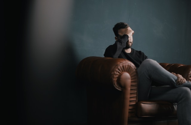 Man on leather couch covering face giving a feeling of sadness and despair. Marble Wellness is a therapy practice in Ballwin Mo offering counseling for men's mental health.