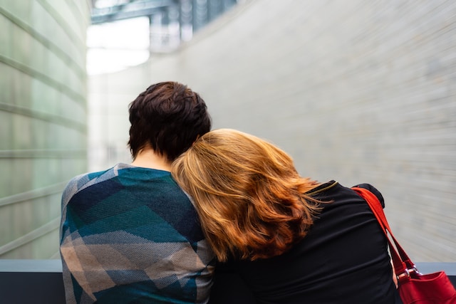 A woman rests her head on another person's shoulder on a bench. Building a support system can help with grief. West County therapists can provide coping strategies to help with grief.
