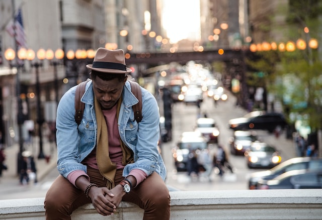 Man with a hat and backpack sits on the ledge of a walkway in a busy city deep in thought. Counseling for men in St. Louis is available in-person and online. Call today to get started.