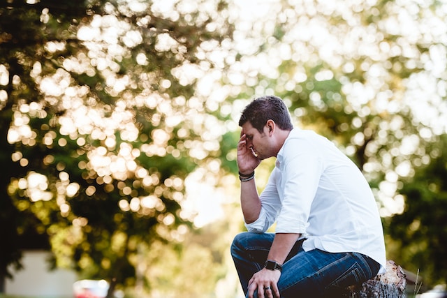 Man in white collared shirt sitting on tree stump appearing to be upset. Therapy for men can create lasting change and improve your mental well-being. Call to schedule a meeting with a counselor specializing in men's mental health.