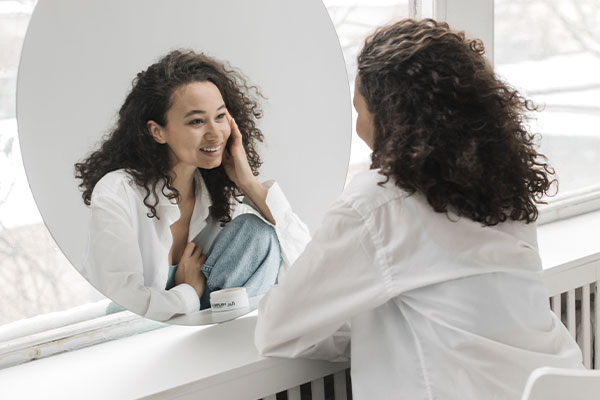 Photo of a woman smiling to her reflection in the mirror. Through counseling for depression in Chicago, IL you can build a positive self-image and self-perception.