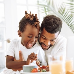 Young son sitting on Dad's lap while they are eating breakfast. It is important for Dad's to make mental health a priority. Schedule an appointment with a St. Louis counselor today.