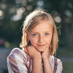 A young girl looks at the camera. Mental health support for kids is available through play therapy in West County, MO at Marble Wellness. Child therapy is available for kids, preteens, and teens.