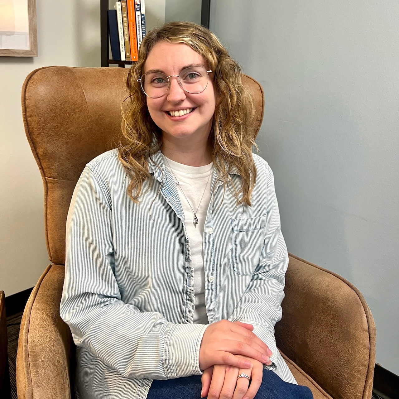 Marble Wellness Therapist Katie, sitting on a chair in the Ballwin MO therapy clinic looking at the camera. Meet with a Missouri online therapist for children, teens young adults, moms and more here!