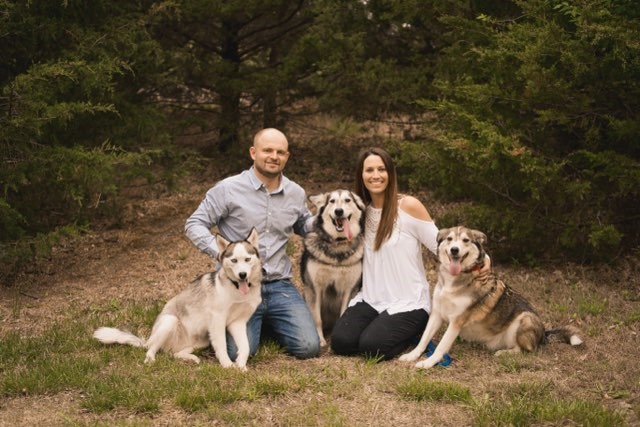 Marble Wellness therapist Deidre smiling at the camera with her husband and dogs. Meet with a Missouri trauma therapist for moms, dads, young adults, and more here! EMDR therapy, PTSD treatment, and more are available in Ballwin, MO with Deidre.